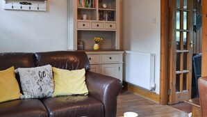 A living room with a brown leather sofa, a coffee table, and a bookshelf. - 2 bedroom accommodation in Penmachno, near Betws-Y-Coed (Penmachno, near Betws-Y-Coed)