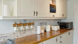 Een keuken met witte kastjes, een houten aanrechtblad en diverse apparaten, waaronder een broodrooster en een magnetron.