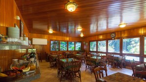 Interior de madera con mesas y sillas, un mostrador con alimentos y grandes ventanales que dan a zonas verdes.