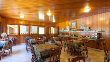 A wooden-paneled dining area with tables and chairs, a kitchen counter with appliances, and a view through the windows.