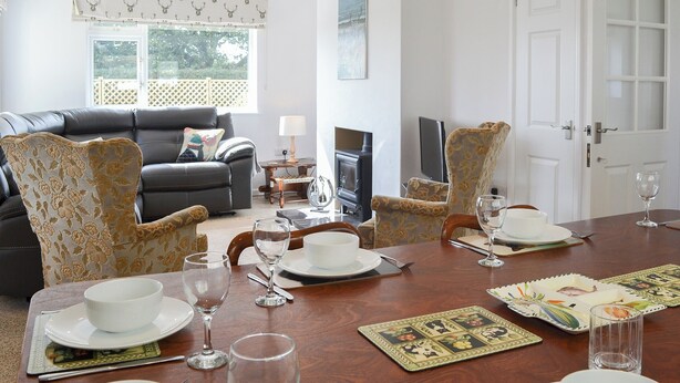 A dining area with a wooden table set for four, a black leather sofa, and patterned armchairs. - 4 bedroom accommodation in Nomansland, near Tiverton (Nomansland, near Tiverton)