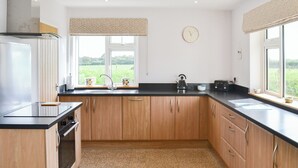 A modern kitchen with wooden cabinets, a black countertop, a stainless steel kettle, and a window with a view of greenery. - 4 bedroom accommodation in Nomansland, near Tiverton (Nomansland, near Tiverton)