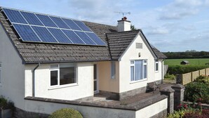 A house with solar panels on the roof, a chimney, and a small garden with a bench. - 4 bedroom accommodation in Nomansland, near Tiverton (Nomansland, near Tiverton)