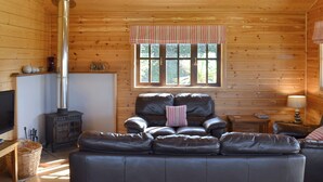 L’intérieur d’un chalet accueillant, avec une cheminée, un canapé en cuir et une fenêtre donnant sur un paysage verdoyant.