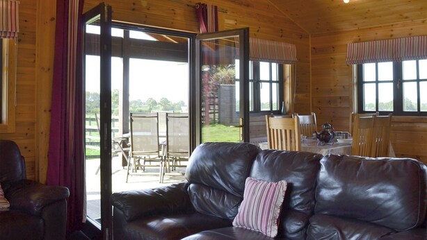 L’intérieur d’un chalet en bois, avec un canapé en cuir, une table à manger et des chaises, et une vue sur l’extérieur.