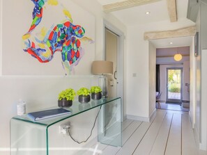Un couloir moderne avec une console en verre, une peinture abstraite aux couleurs vives et une vue sur l’espace salle à manger.