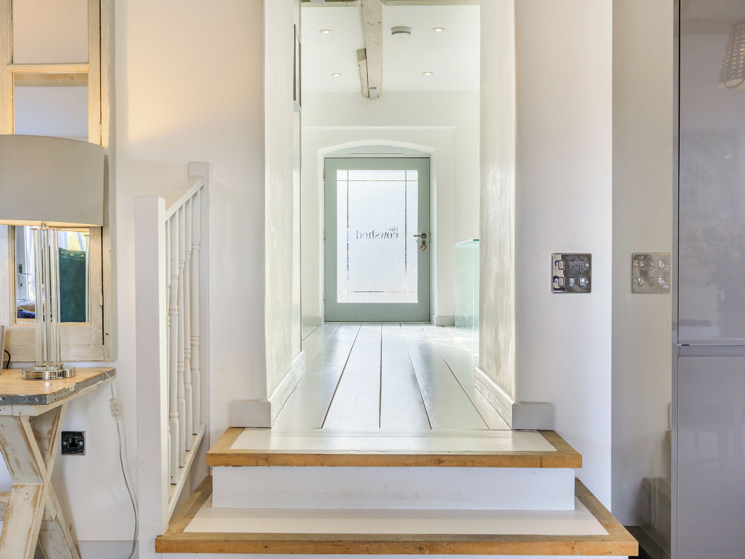 A hallway with a wooden staircase leading to a door with a frosted glass window.