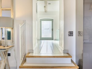 Un pasillo con una escalera de madera que lleva a una puerta con un ventanal satinado.