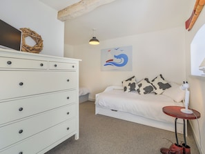 Een slaapkamer met een witte dressoir, een bed met kussens met koeienprint, een kunstwerk aan de muur en een tafeltje met een lamp.
