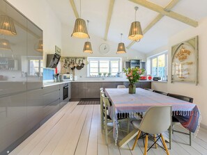 Een moderne keuken met een eethoek, met een groot kookeiland, hangende pannen en een klok aan de muur.