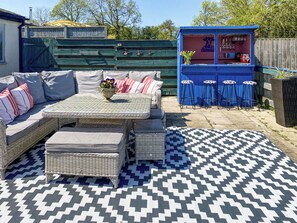 Un patio con un conjunto de sofá de mimbre, una pequeña barra con taburetes y una alfombra estampada.