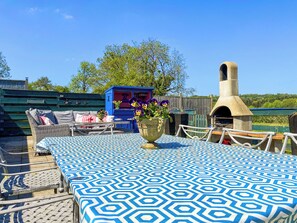 A patio with a patterned tablecloth, wicker furniture, a blue cabinet with flowers, and a brick oven.