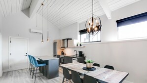 A modern kitchen with a dining area, featuring a wooden table, black chairs, and pendant lighting.