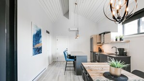 A modern kitchen with a wooden dining table, a blue chair, and a pendant light.