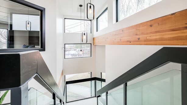 A modern interior with glass railings, wooden paneling, and multiple windows providing natural light.