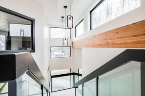 A modern interior with glass railings, wooden paneling, and multiple windows providing natural light.