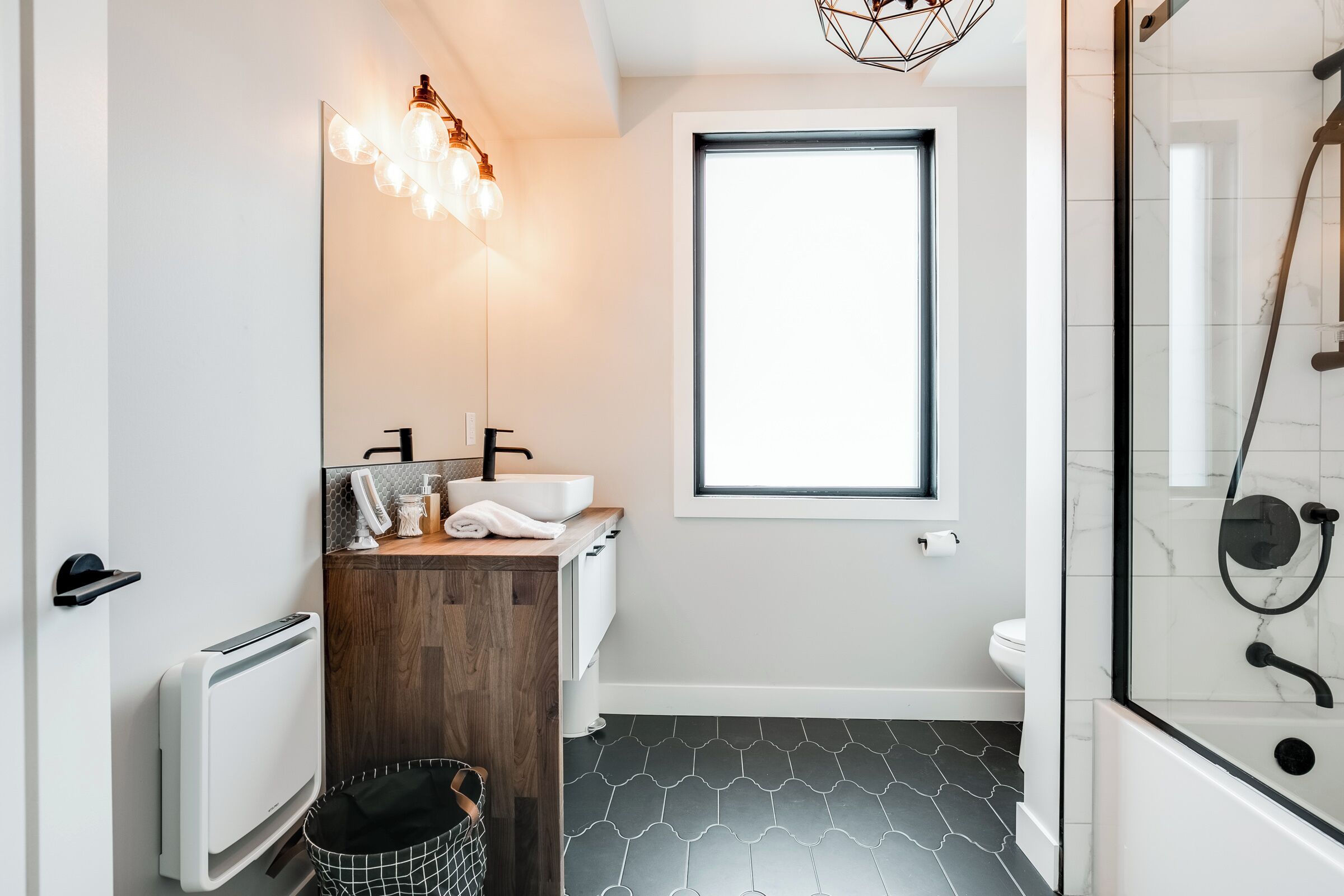Une salle de bain moderne avec un meuble-lavabo en bois, un grand miroir, une douche en verre et un carrelage noir et blanc à motifs.