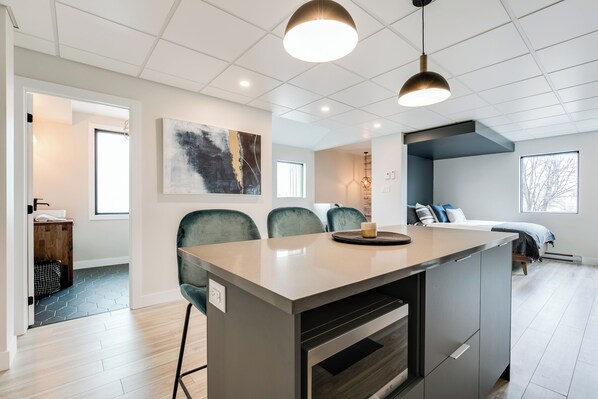 A modern kitchen with a central island, recessed ceiling lights, and a large window.