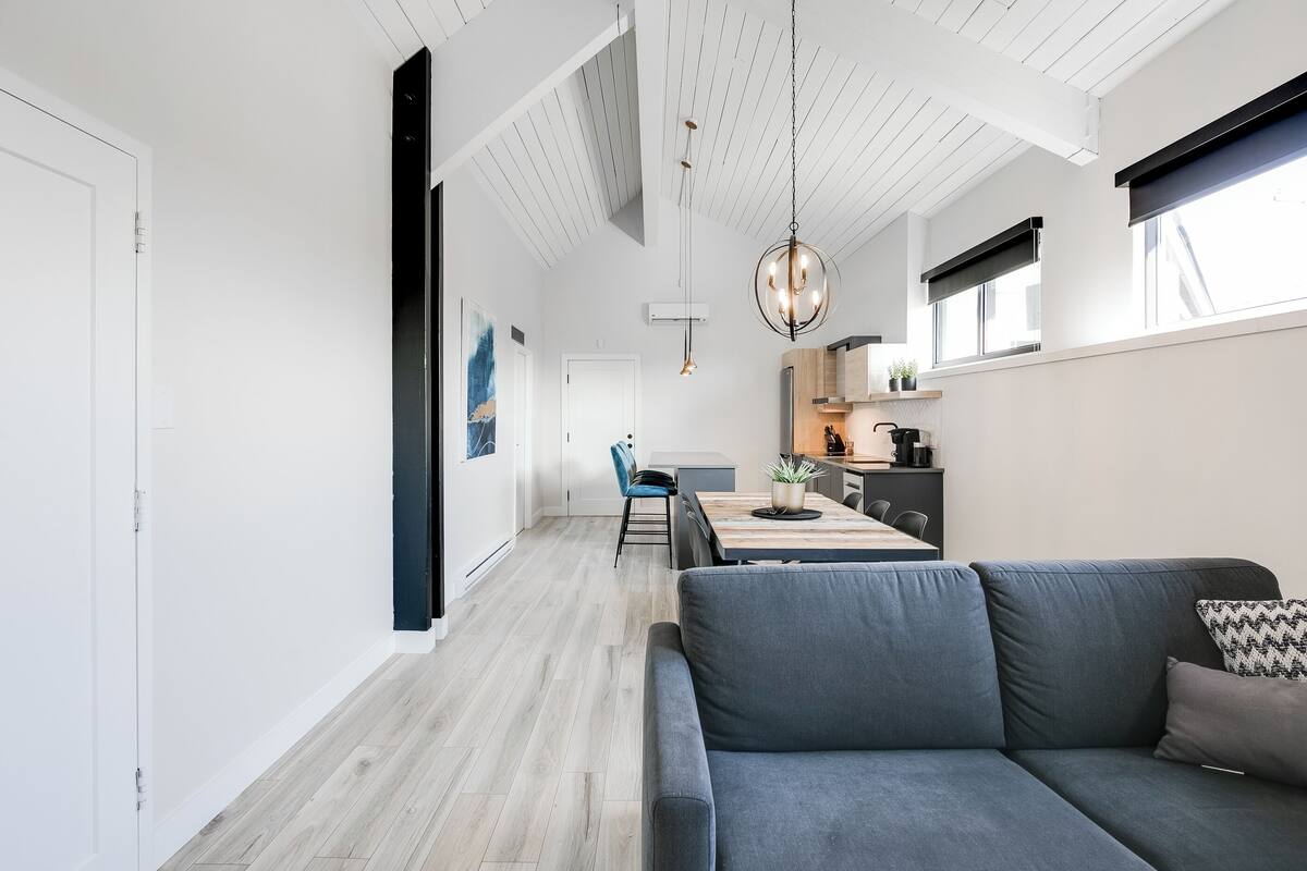 A modern interior with a grey sofa, a dining area, and a kitchen.