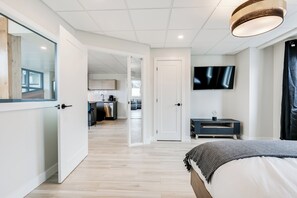 A modern hotel room with a bed, a TV mounted on the wall, and a view into the kitchen area.