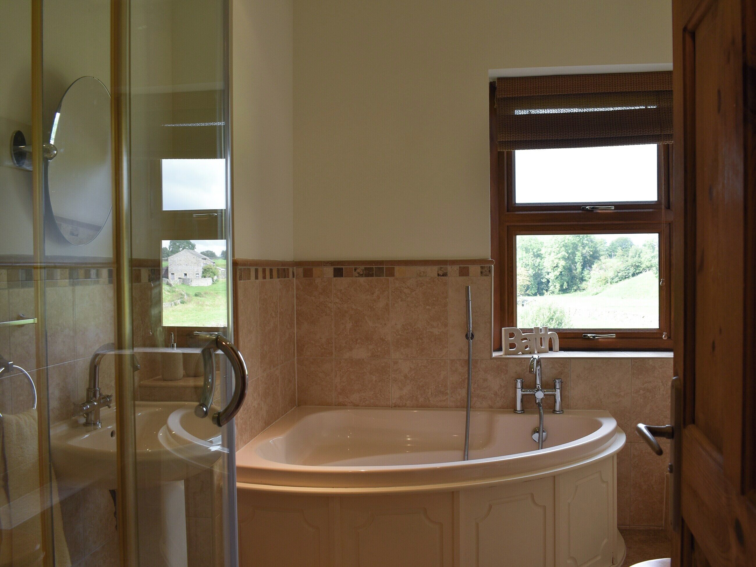 Ein Badezimmer mit freistehender Badewanne, einer Duschkabine aus Glas und einem Fenster mit Blick auf Grünflächen.