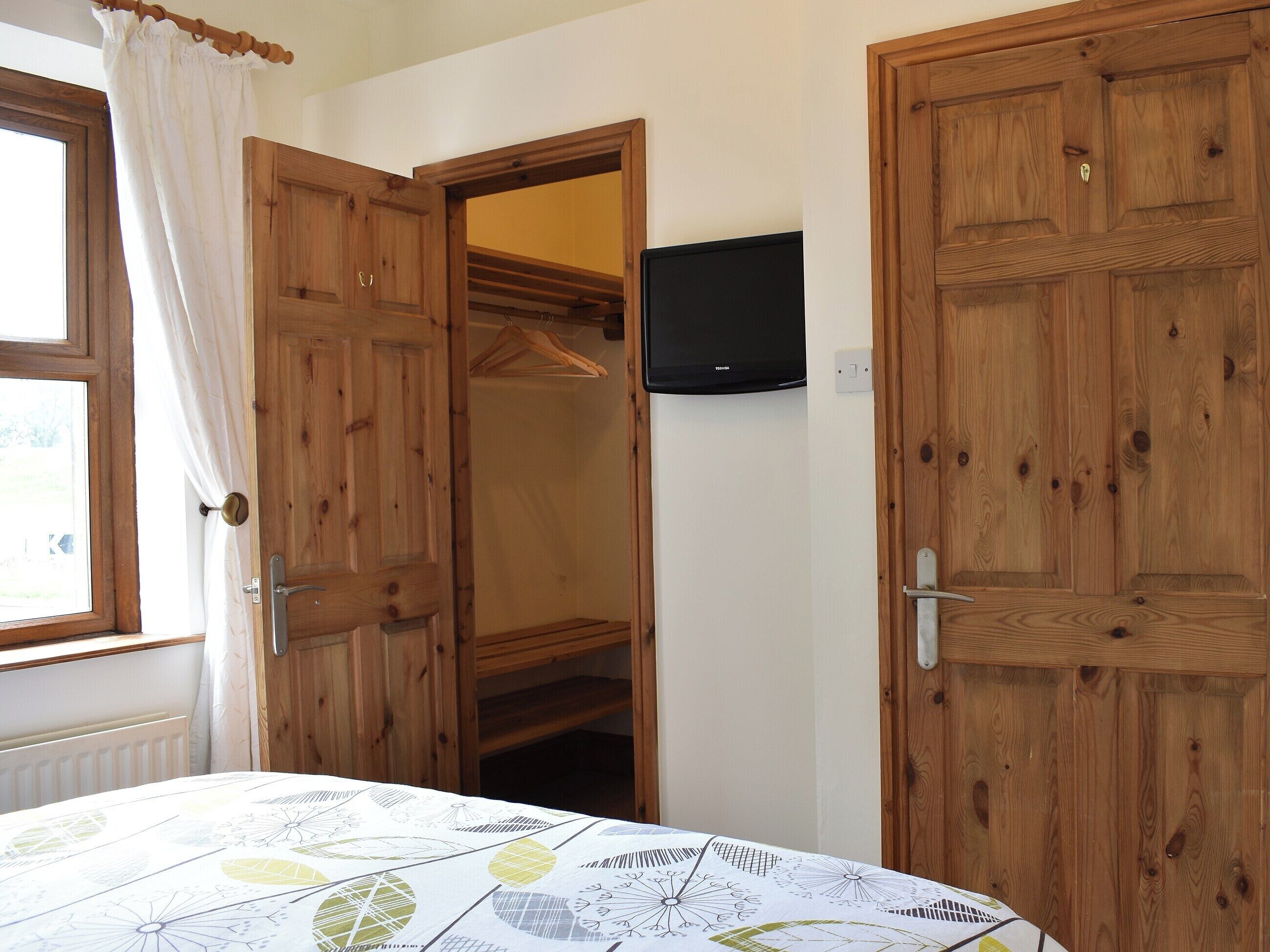 Ein Schlafzimmer mit Bett, Holzschrank und Fernseher an der Wand.