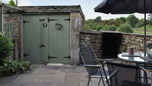A stone building with a green door, a heart-shaped decoration, and a table with chairs and an umbrella. - 3 bedroom accommodation in Long Preston, near Settle (Long Preston, near Settle)