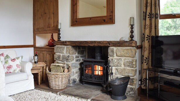 A cozy living room with a stone fireplace, a television, and a floral-patterned window curtain. - 3 bedroom accommodation in Long Preston, near Settle (Long Preston, near Settle)