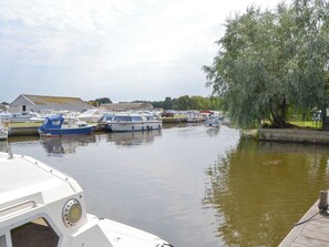 A marina with several boats docked, a weeping willow tree, and a building in the background.