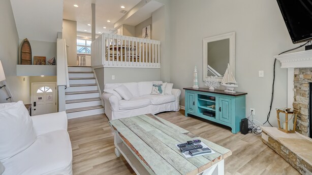 A spacious living area with a white sofa, a wooden coffee table, and a teal cabinet. A staircase with white railings leads to an upper level. - Beautiful Townhome 2 Blocks from the beach with beach cruisers! (Jacksonville Beach)