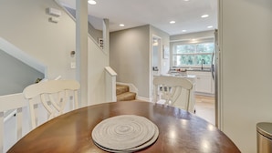 A dining area with a wooden table and chairs, a staircase leading to a kitchen, and a view of the outside through a window. - Beautiful Townhome 2 Blocks from the beach with beach cruisers! (Jacksonville Beach)