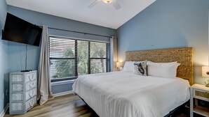 A bedroom with a bed, a TV, a ceiling fan, a window with blinds, and a nightstand. - Beautiful Townhome 2 Blocks from the beach with beach cruisers! (Jacksonville Beach)