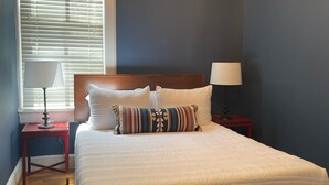 Un dormitorio con una cama grande, una ventana con persianas, una mesita de noche con lámpara y una moderna lámpara de araña.