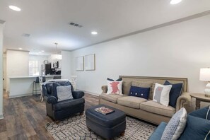 Un salon moderne avec un canapé, un fauteuil, un pouf et un coin repas à l’arrière-plan.