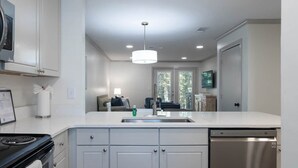 Une cuisine moderne avec des meubles blancs, une cuisinière encastrée, un lave-vaisselle et un luminaire suspendu.