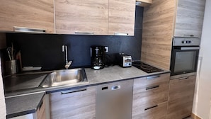 A modern kitchen with wooden cabinets, a stainless steel sink, a coffee maker, a toaster, and an oven. - SAPAUDIA G – Ski-in/ski-out apartment, lovely view – Parking (La Clusaz)