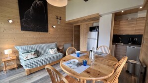 A cozy cabin interior with a wooden dining table, chairs, a sofa, a kitchen area, and a bear mural on the wall. - SAPAUDIA G – Ski-in/ski-out apartment, lovely view – Parking (La Clusaz)