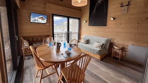 A wooden cabin interior with a dining table, chairs, a sofa, and a large window offering a mountain view. - SAPAUDIA G – Ski-in/ski-out apartment, lovely view – Parking (La Clusaz)