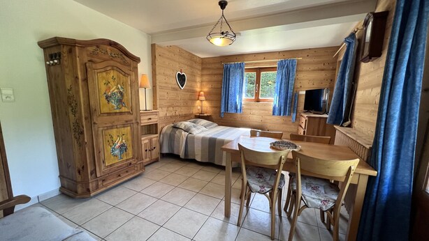 Una stanza accogliente con un letto, un armadietto in legno, un tavolo da pranzo con sedie e una televisione.