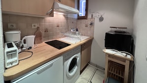 Una cucina compatta con lavatrice, macchina da caffè e un piccolo tavolo di legno.
