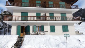 Un edificio de varios pisos con balcones y contraventanas verdes, rodeado de nieve.