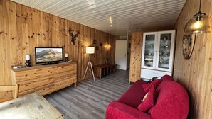 Een gezellig houten interieur met een televisie, een lamp, een rode bank en een eethoek.