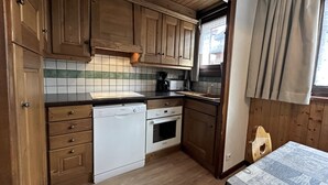 Une cuisine de taille réduite, dotée de meubles en bois, d’un lave-vaisselle, d’un four et d’une fenêtre avec des rideaux.