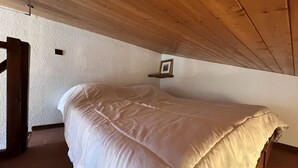A bedroom with a bed, wooden ceiling, and a small shelf with a picture. - RICHEMONT 12 – Duplex near the slopes with village views – Garage (La Clusaz)