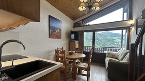 A cozy kitchen with a sink, wooden chairs, a dining table, and a large window offering a scenic view. - RICHEMONT 12 – Duplex near the slopes with village views – Garage (La Clusaz)