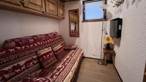 A cozy room with a patterned sofa, wooden cabinets, a mirror, a lamp, and a window. - RICHEMONT 12 – Duplex near the slopes with village views – Garage (La Clusaz)