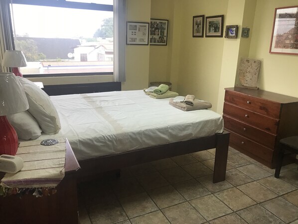 A bedroom with a bed, a dresser, a window with a view, and a wall with framed pictures.