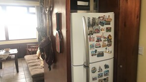 A kitchen with a refrigerator covered in magnets, a wooden cabinet, a sofa, and a dining table. - Deluxe Two-Bedroom Penthouse Apartment in Escalante, San Jose Center (San José)