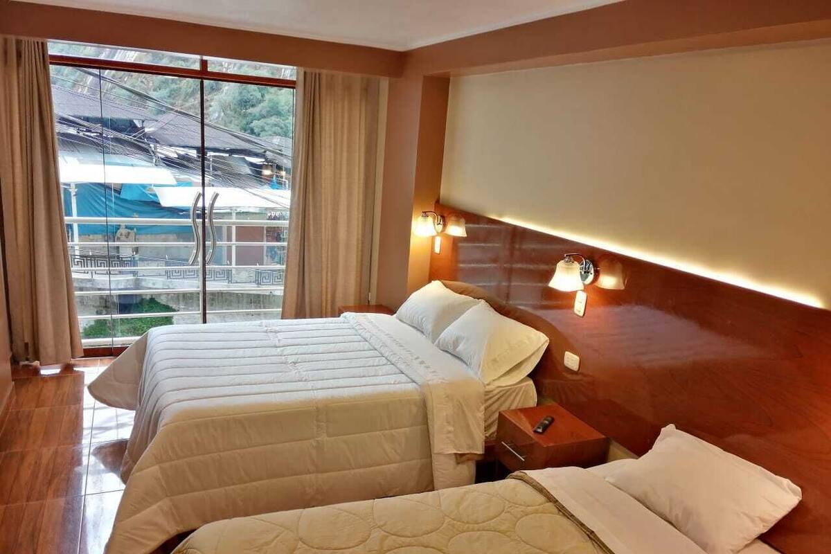 Habitación de hotel con dos camas, un ventanal con cortinas y vistas al exterior.