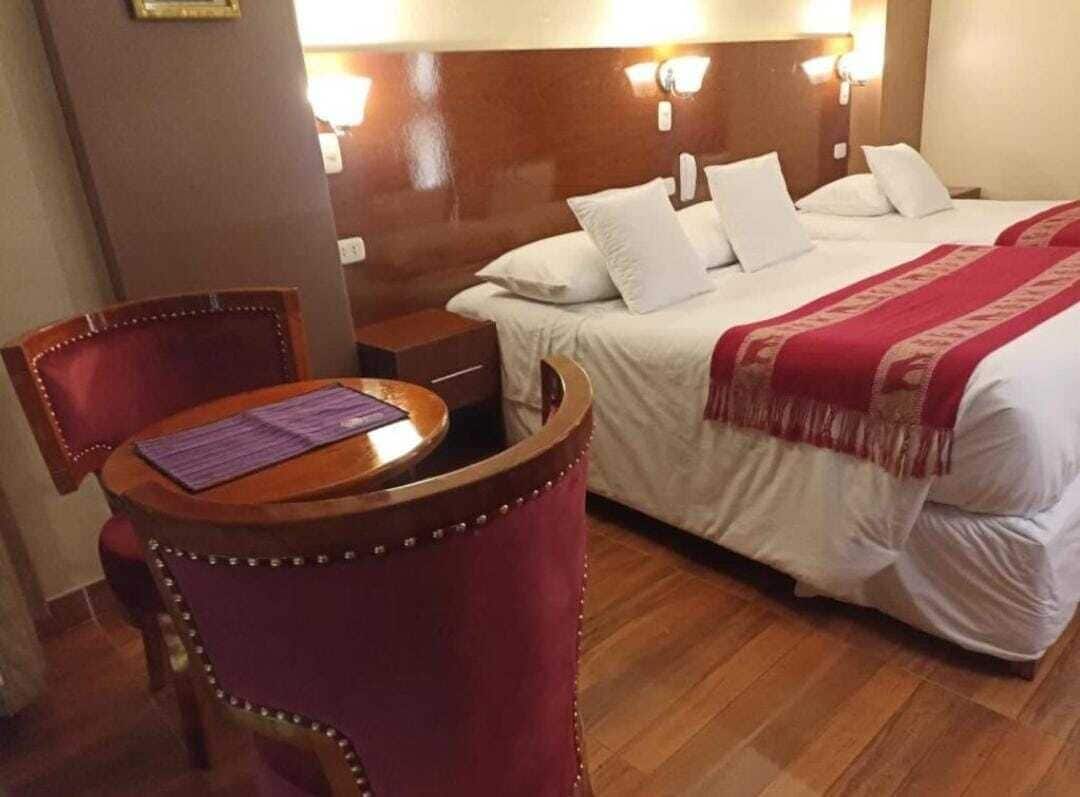 Una habitación de hotel con una cama, una mesita de noche de madera, una silla morada y una pequeña mesita auxiliar.